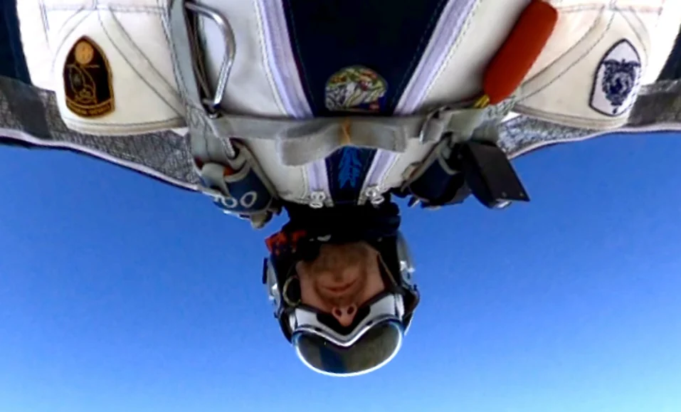 Personne équipée d’un casque, de lunettes et d’un harnais, vue inversée sur fond de ciel bleu